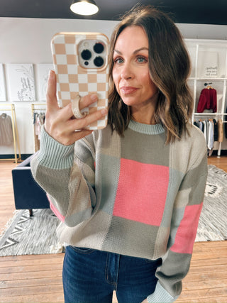 Woman taking a selfie wearing a checkered sweater in a clothing store.