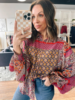 Woman taking a mirror selfie wearing a colorful patterned blouse in a clothing store.
