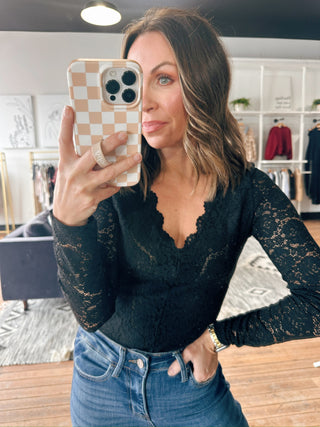 Woman taking a mirror selfie wearing a black lace top and blue jeans in an indoor setting.