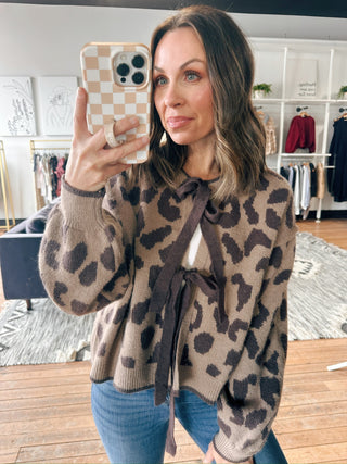 Woman wearing a leopard print sweater taking a selfie in a clothing store.