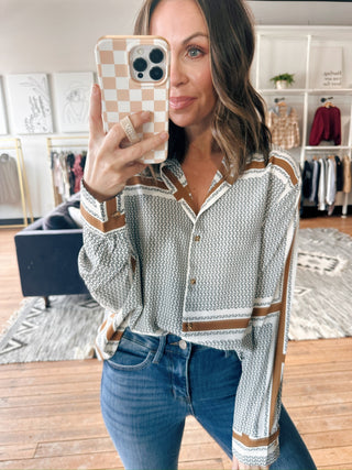 Woman taking a mirror selfie wearing a patterned blouse and jeans in a room with furniture and decor.
