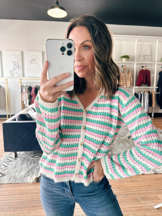 Woman taking a mirror selfie wearing a striped cardigan in a clothing store.