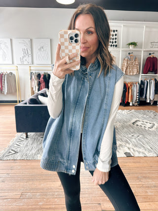 Woman taking a mirror selfie wearing a denim vest in a clothing store.