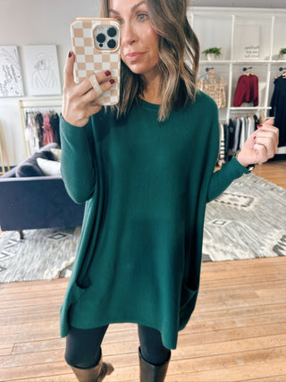 Woman taking a mirror selfie wearing a green sweater in a store.