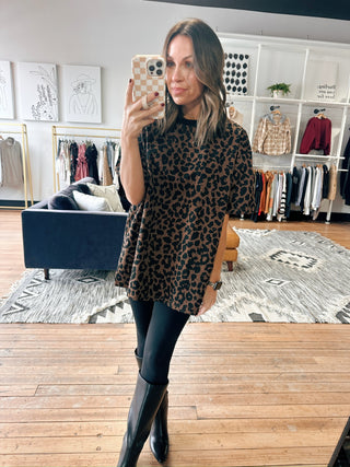 Woman taking a mirror selfie wearing a leopard print dress in a clothing store.