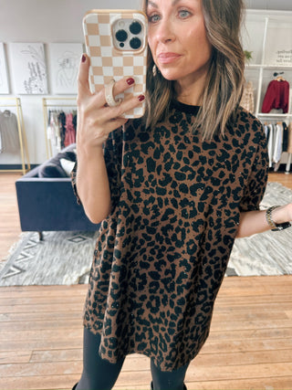 Woman wearing a leopard print dress taking a mirror selfie in a room with furniture.