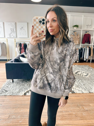 Woman taking a mirror selfie wearing a patterned jacket in a room with clothing racks.