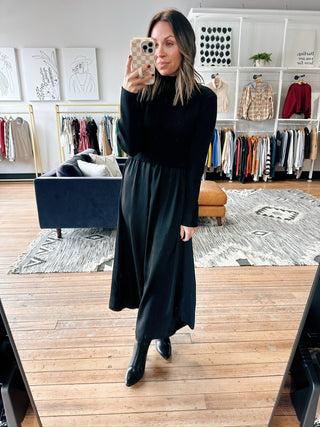 Woman taking a mirror selfie wearing a black dress in a clothing store.