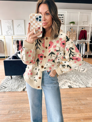 Woman taking a mirror selfie wearing a floral cardigan and jeans in a store.