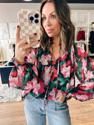 Woman taking a mirror selfie wearing a floral blouse and jeans in a clothing store.