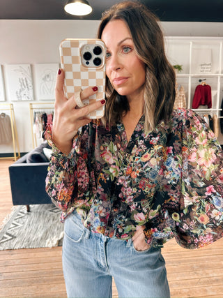 Woman taking a mirror selfie wearing a floral blouse and jeans in a room with decor.