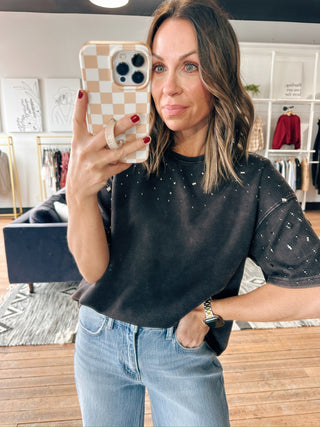 Woman taking a mirror selfie wearing a black top with white patterns and light blue jeans.