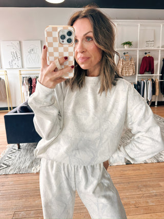 Woman taking a mirror selfie wearing a white outfit in a room with clothing racks.