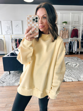 Woman taking a mirror selfie wearing a yellow sweatshirt in a clothing store.
