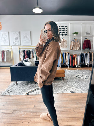 Woman taking a mirror selfie in a clothing store with racks of clothes in the background.