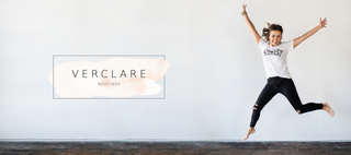 VerClare Boutique Logo. Owner Cristina Jumping, she is wearing black distressed skinny jeans and a white graphic tee that reads "midwest". 